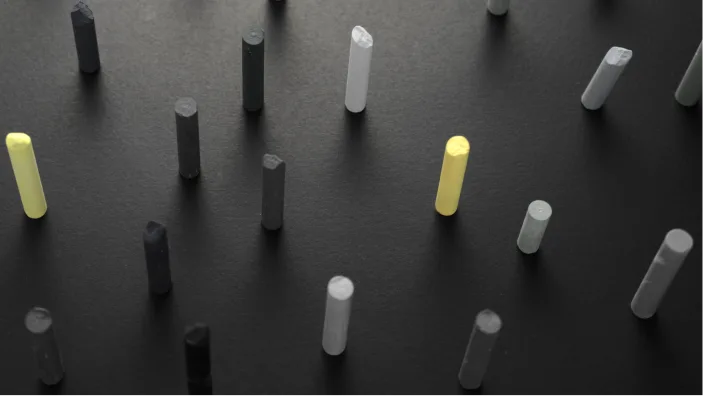 Pastel sticks standing upright on a dark surface, two of them yellow